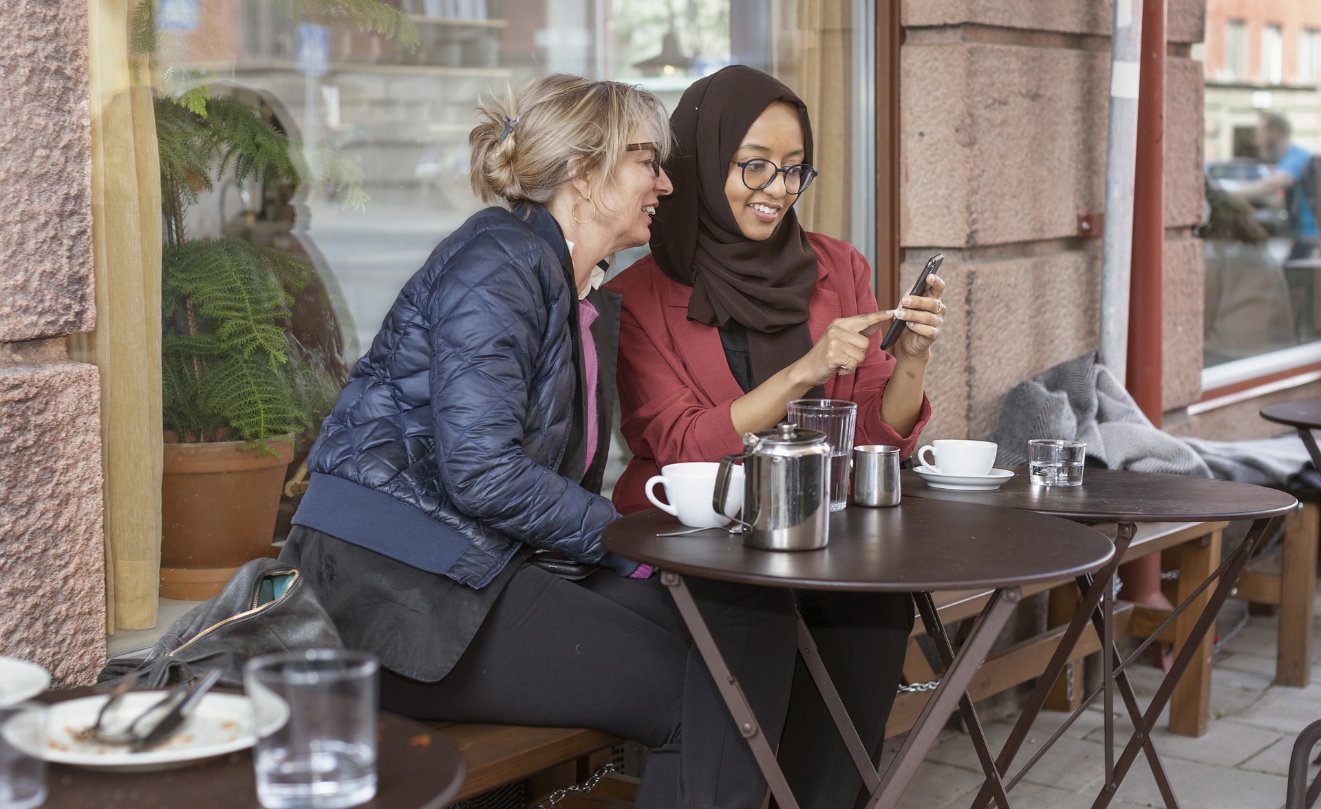 2 kvinnor fikar och tittar på smartphone på cafè utomhus