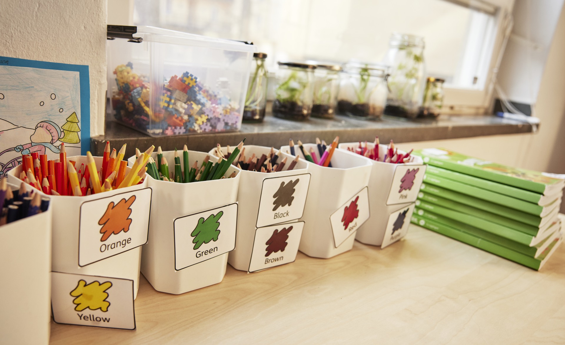 Pennor sorterade färgvis i pennställ på bord i klassrum.