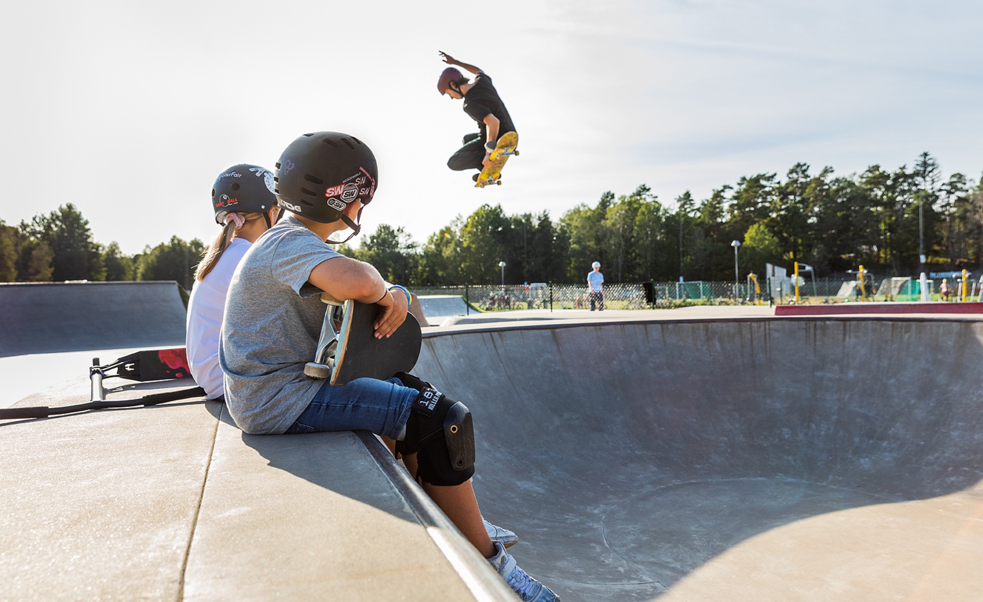 Barn tittar på när äldre kille hoppar med skateboard i skateparken i Djupedalsäng.