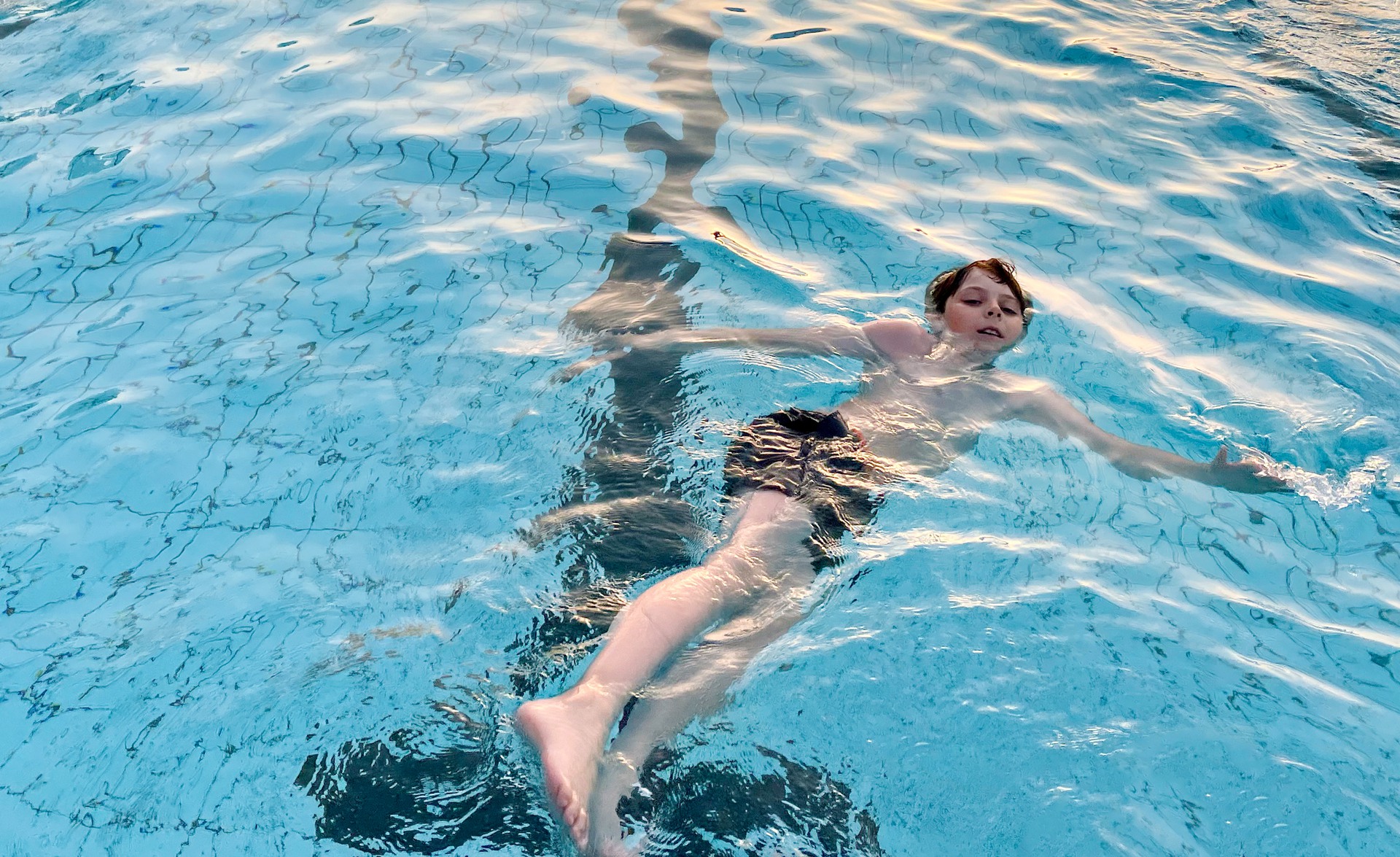 School kid boy splashing in an outdoor swimming pool on warm summer day. Happy healthy preteen child enjoying sunny weather in city public pool. Kids activity outdoors with water