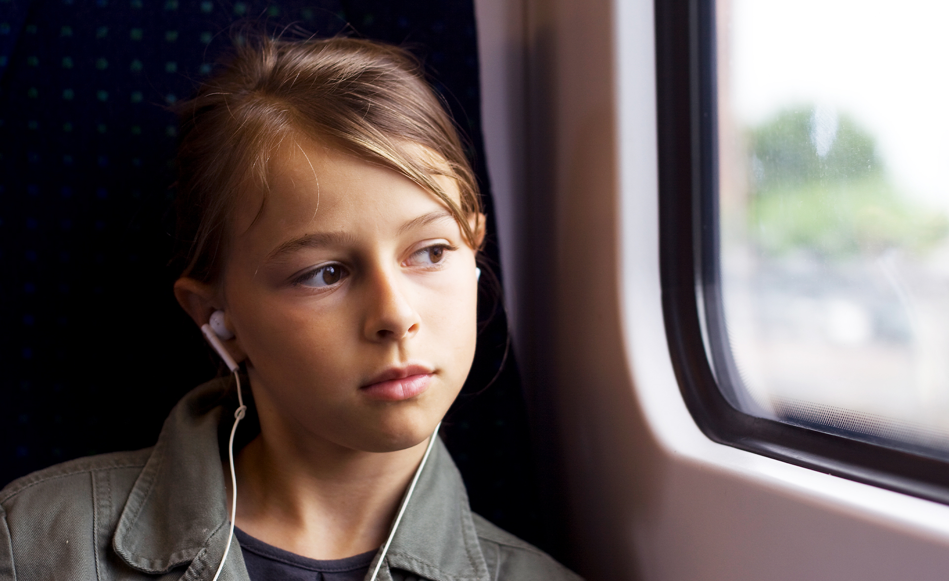Flicka tittar ut genom ett tågfönster, hon har airpods i öronen och brunt hår och bruna ögon.