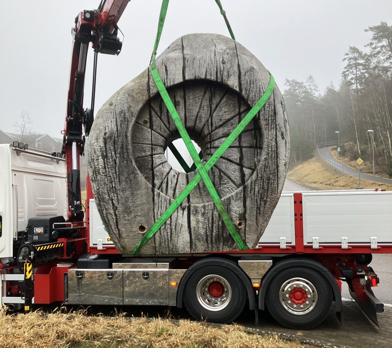 En träskulptur med rund form och ett hål i mitten lyfts upp på ett lastbilsflak