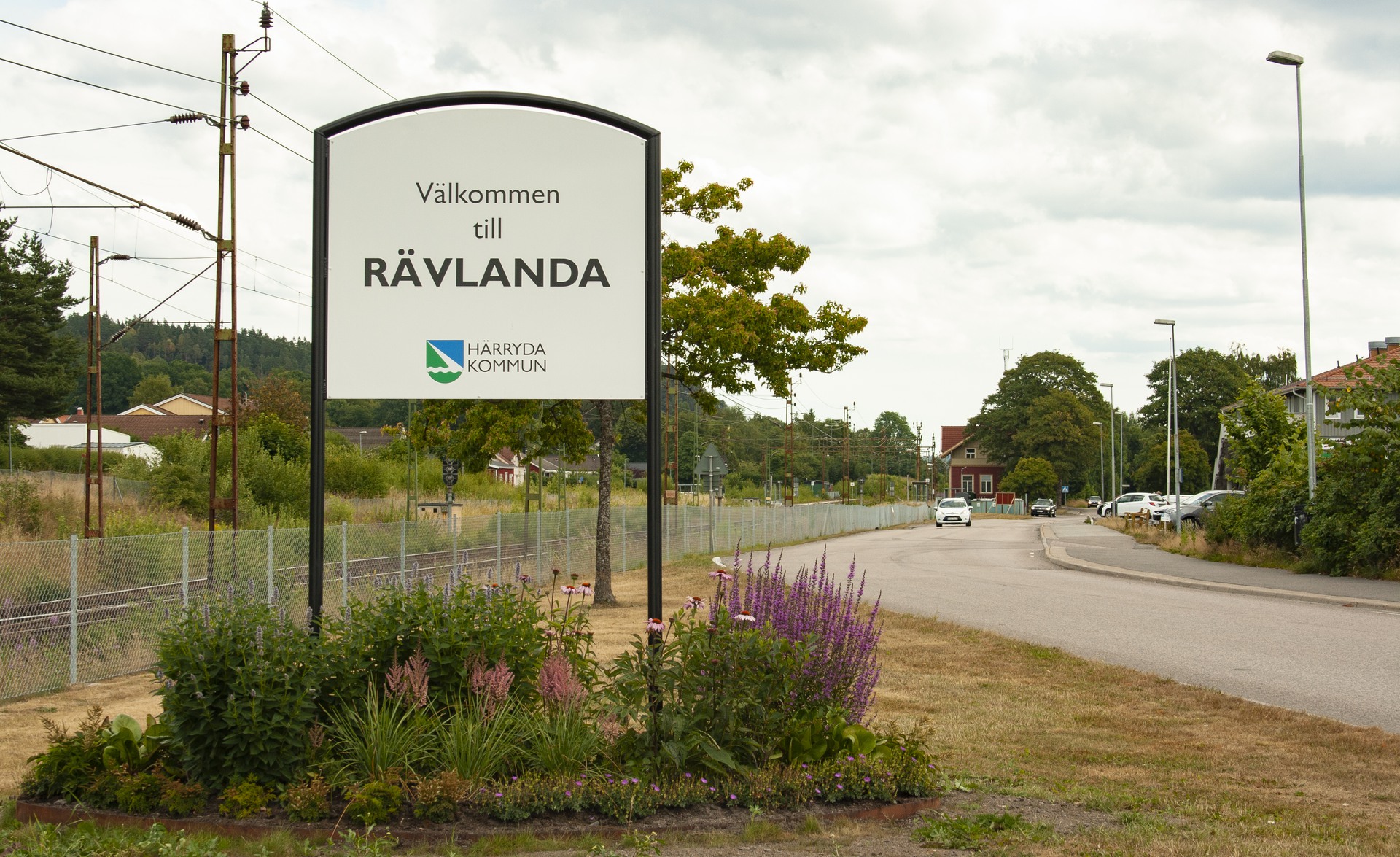 En skylt som säger Välkommen till Rävlanda. Runt skylten finns en blomsterrabatt.