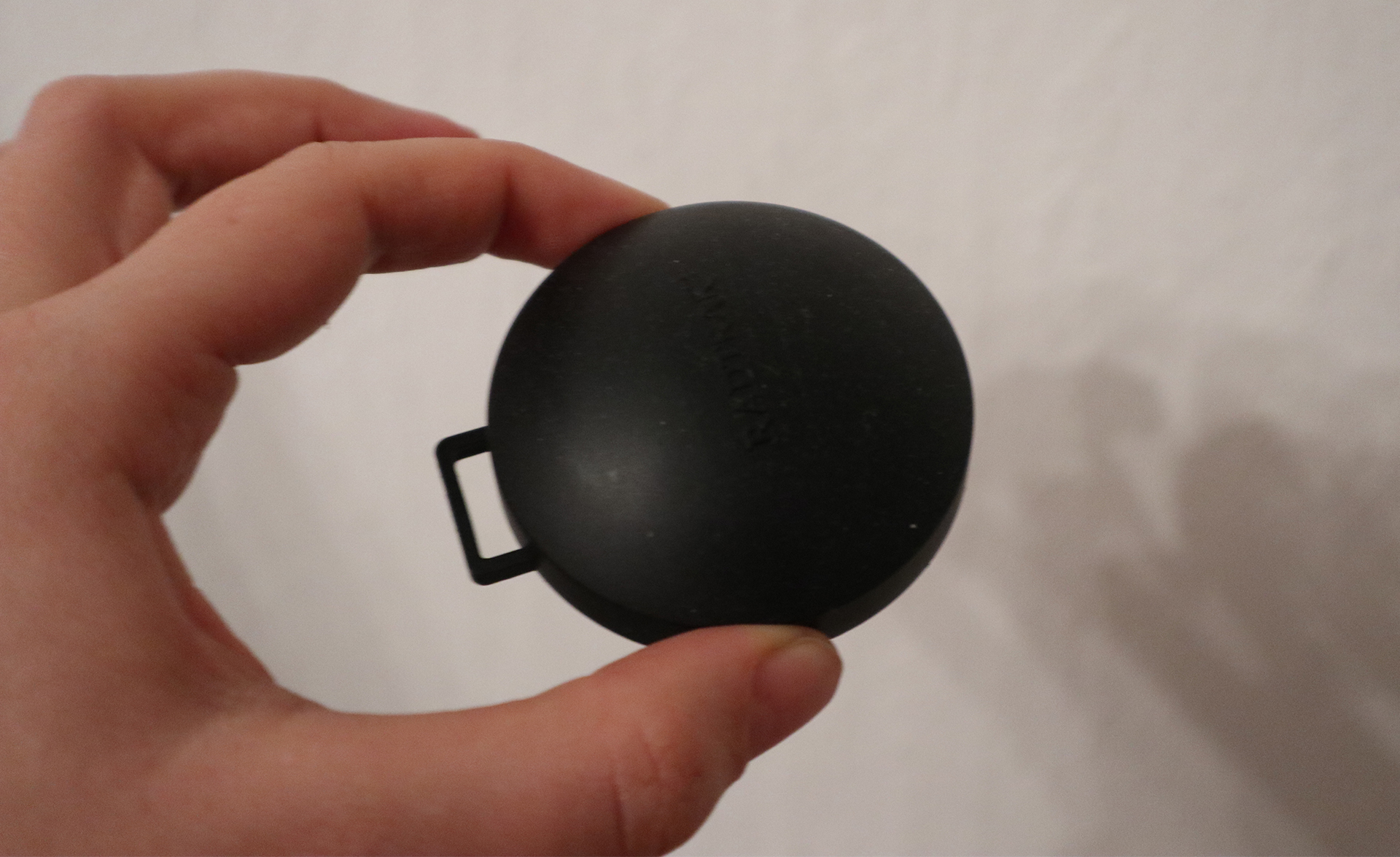 En hand håller i en liten svart puck för radonmätning hemma
