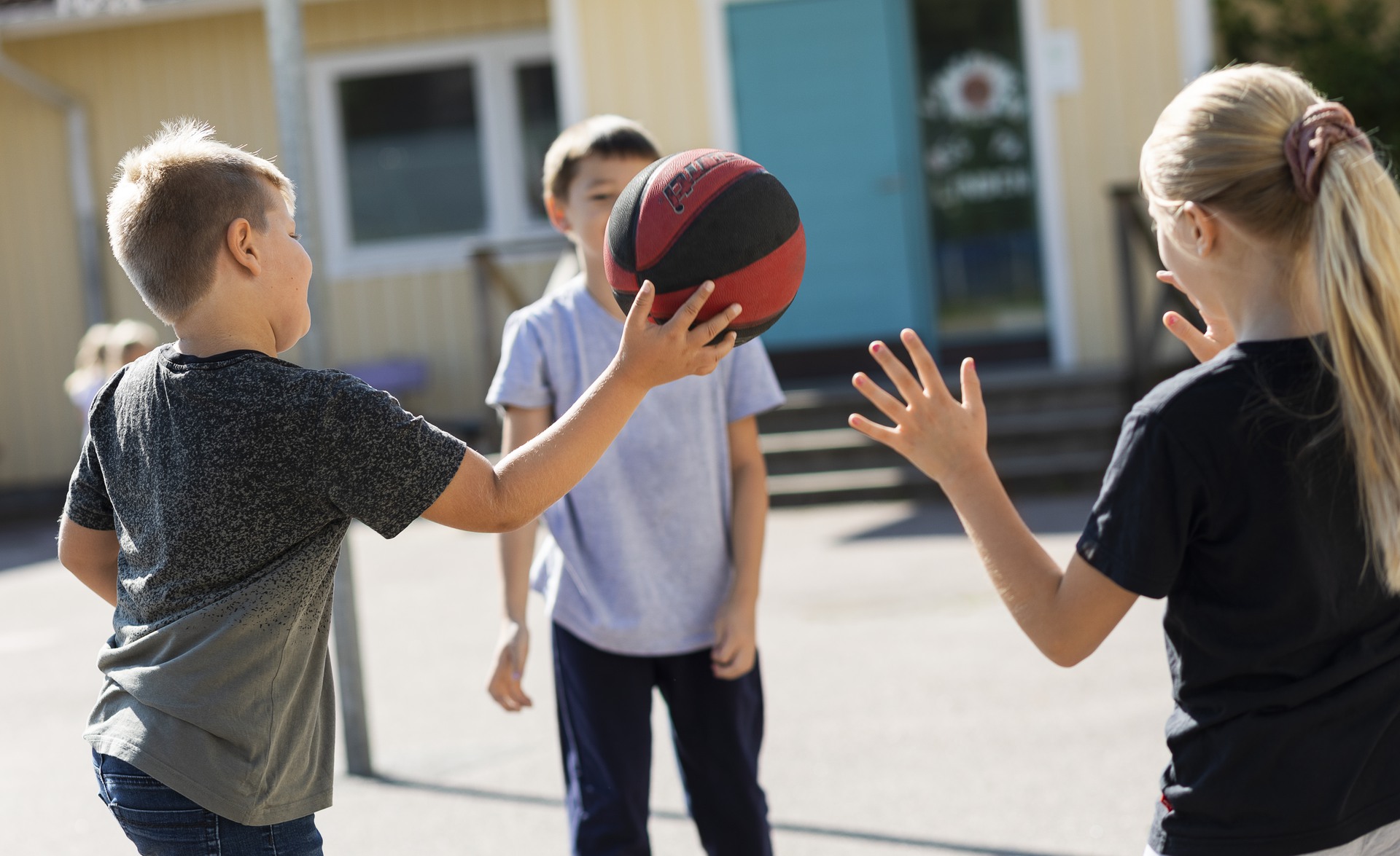 Tre barn står i en ring och leker med en basketboll