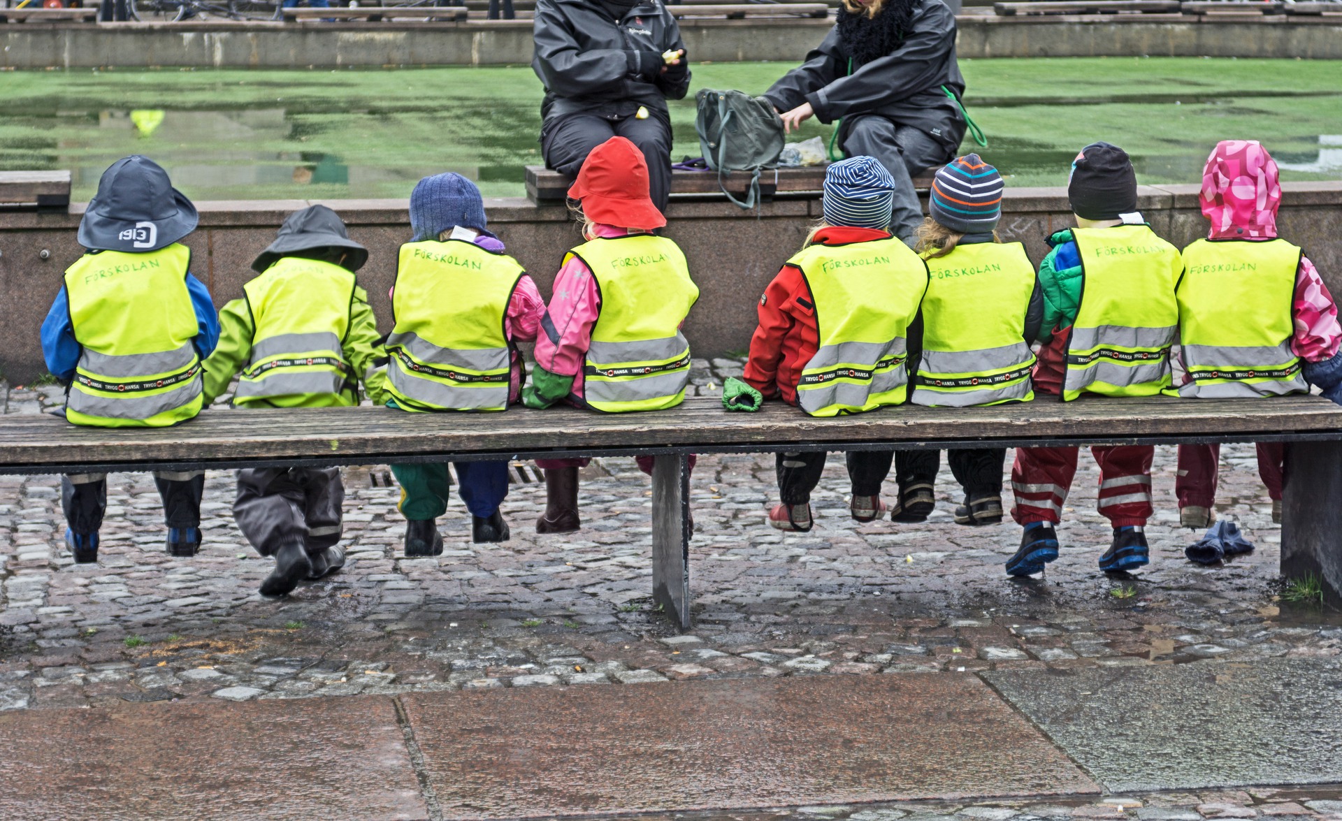 8 barn i reflexväst sitter på en bänk. Det regnar.